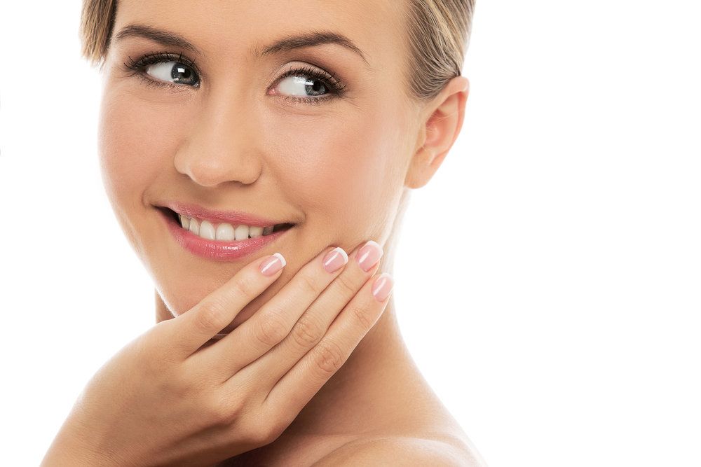 A beautiful woman holding her face looks over her shoulder behind her.