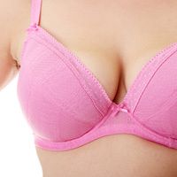 A closeup of a woman with large breasts wearing a pink cotton bra with bow detail.