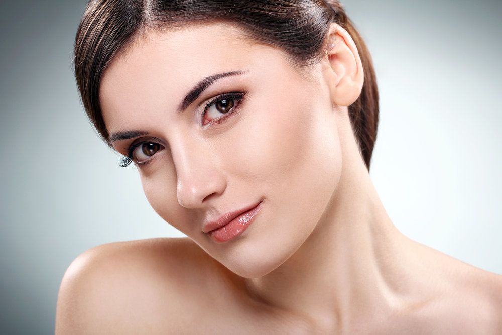 A coy brunette woman with no shirt on leans to teh side with the traces of a smile on her face.